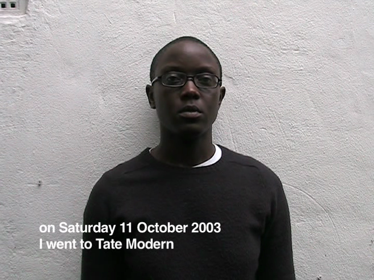 The artist in front of a gallery's white wall. Text on the left bottom writes, On Saturday 11 October 2003 I went to Tate Modern