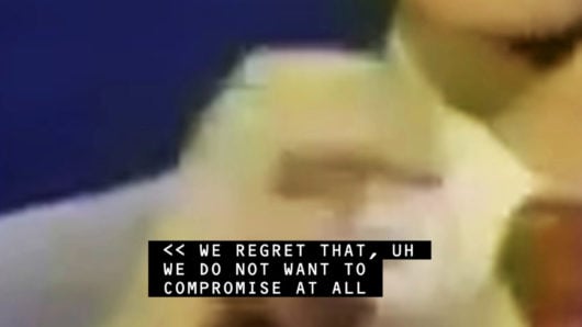 still image from Jenny Brady video 'Receiver', blurry image of hand with overlaid caption that says, "We regret that, um we do not want to compromise at all"