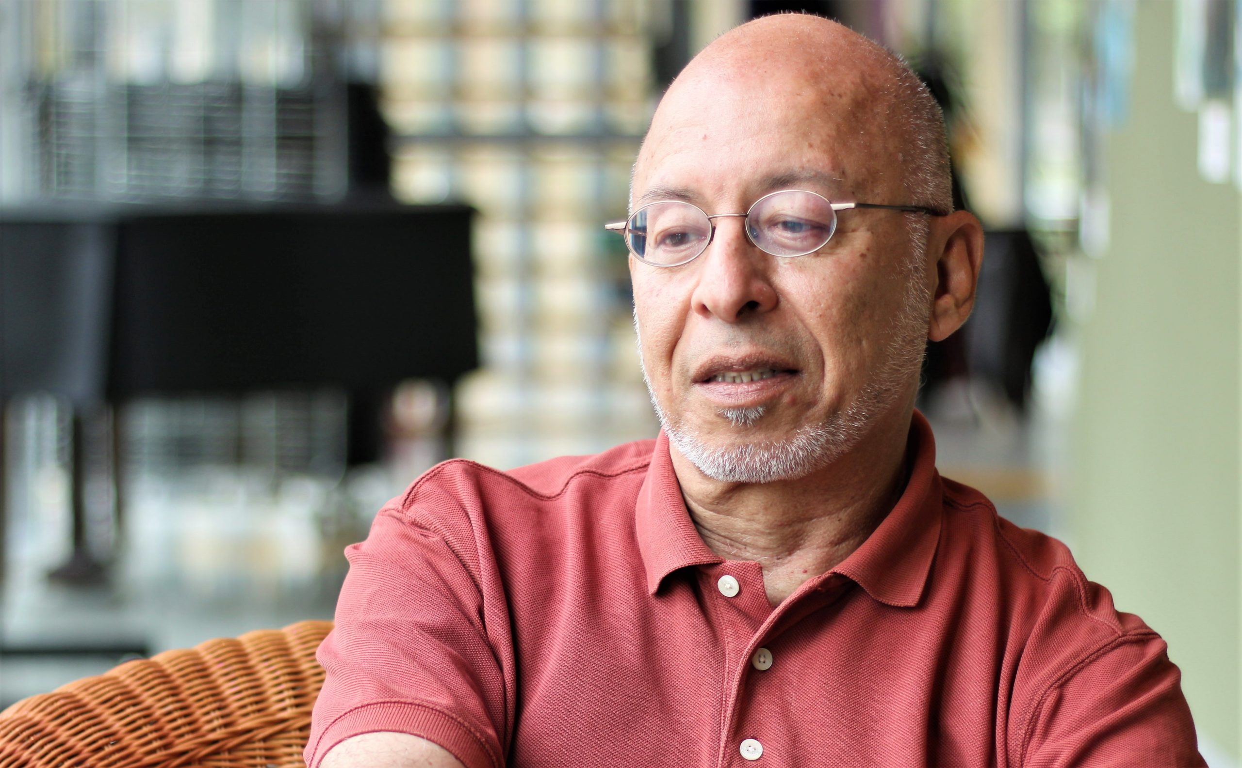 portrait image of filmmaker Andre Reeder, head and shoulders wearing a pink shirt. Middle aged Surinamese man with bald head, glasses and a grey beard