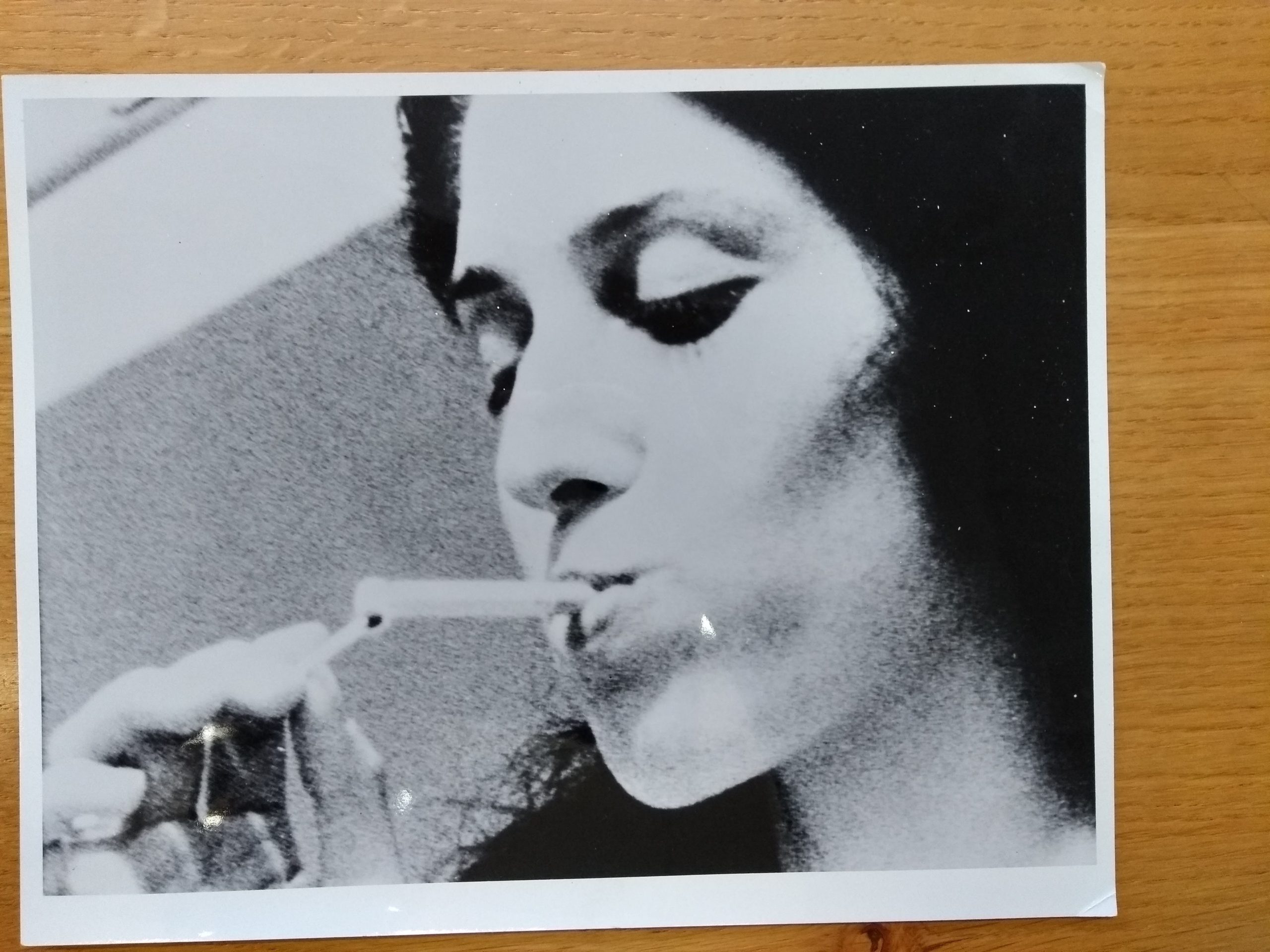 A B&W photograph on a wooden surface. In the picture is a close up of a woman lighting a cigarette with a match.
