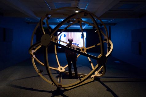 A geodesic globe made with metal structure sits in a dark space. Through this an image of a string instrument is projected on the back wall. 