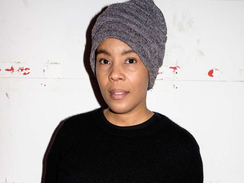 A black person wearing a beanie and a simple long sleeve jumper in a brightly lit space.
