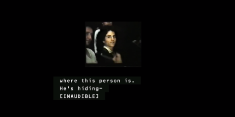 still image of Receiver by Jenny Brady. A small image in the centre of a black screen of a white man with long black curly hair sits in a crowd looking towards the person taking the picture. there is a caption below in white which says 'where this person is. He's hiding- [INAUDIBLE'