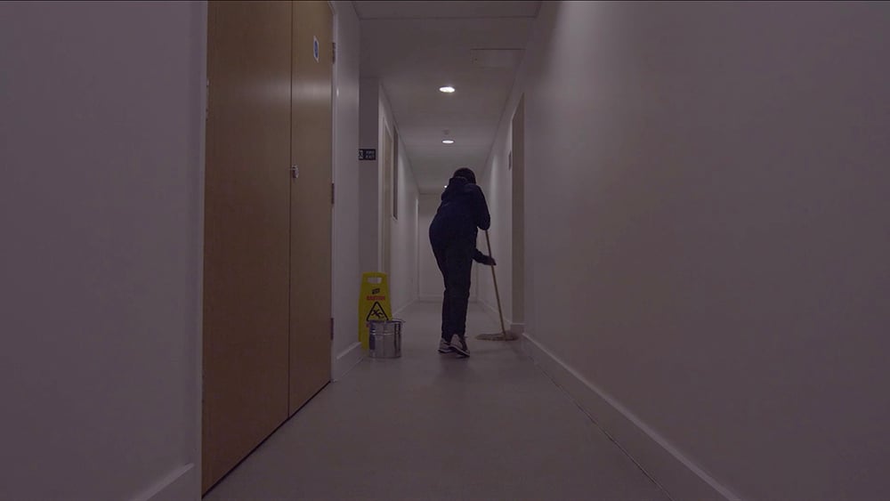 A cleaner is mopping the floor of an empty white corridor. 