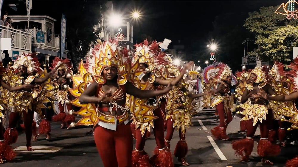 A group of black women in golden costumes parading on the street at night.