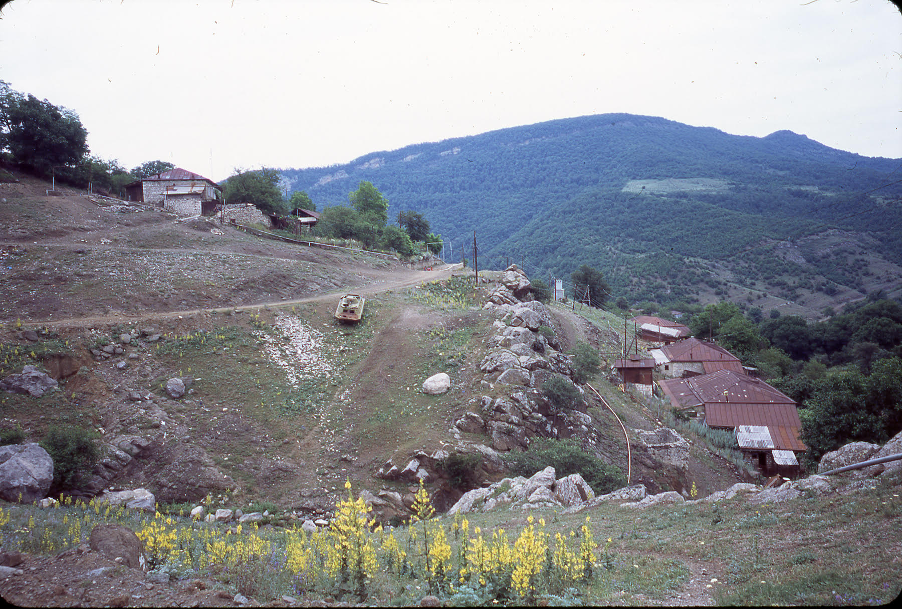 image from the film Black Bach Artsakh (2021), a tank is parked in the middle distance on the side of a hill, it is incongruous in a peaceful rural setting