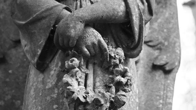 close up on a dusty statue's hands holding a wreath