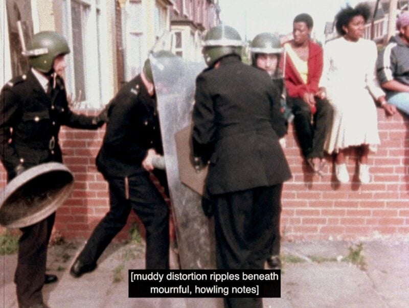 four white police officers with helmets and riot shields are shoving someone down while three black people sitting and watching in the background. The caption reads, muddy distortion ripples beneath mournful, howling notes.