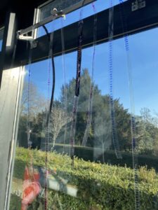 Hand painted film srips are hung over a suspension of a window that looks out to a green park under the blue sky

