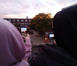 Twop people in hoodies filming a building at sunset with their smartphone and camcorder 
