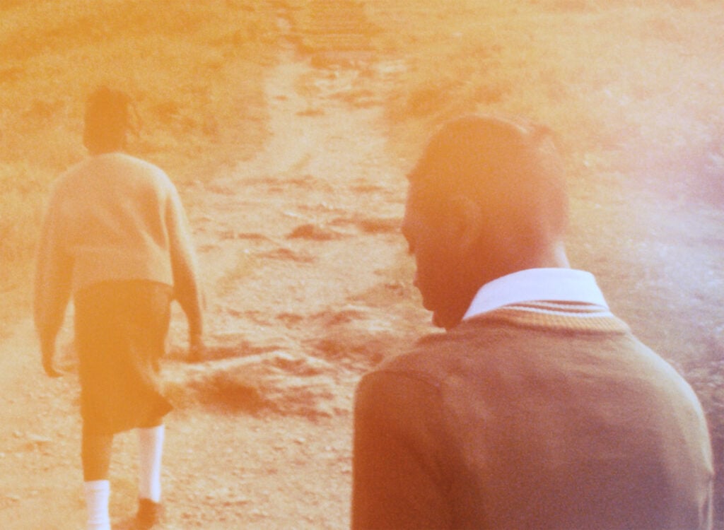 Yellow tinted image shows two black teenagers in school uniforms walking up a hilly road