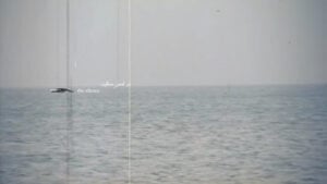 The image shows a serene ocean under a grey sky filling the frame. The horizon line divides the image into two halves, with a white caption that reads 'touch of the silence' followed by Farsi words. The words 'touch of' are partially scratched off.