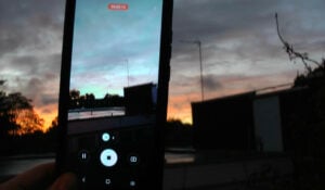 A shaky image of a smartphone video recording the sunset that colours the sky bright orange, yet its colour subdues when viewed through the smartphone.