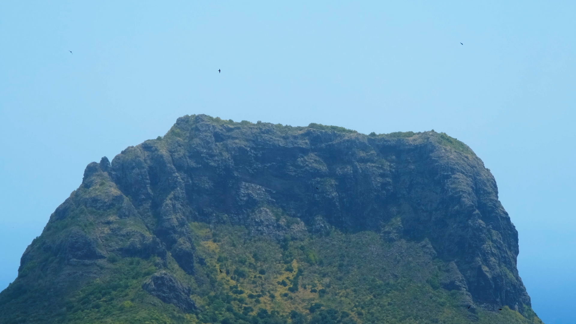 an image of a green verdant rocky hill against a blue sky