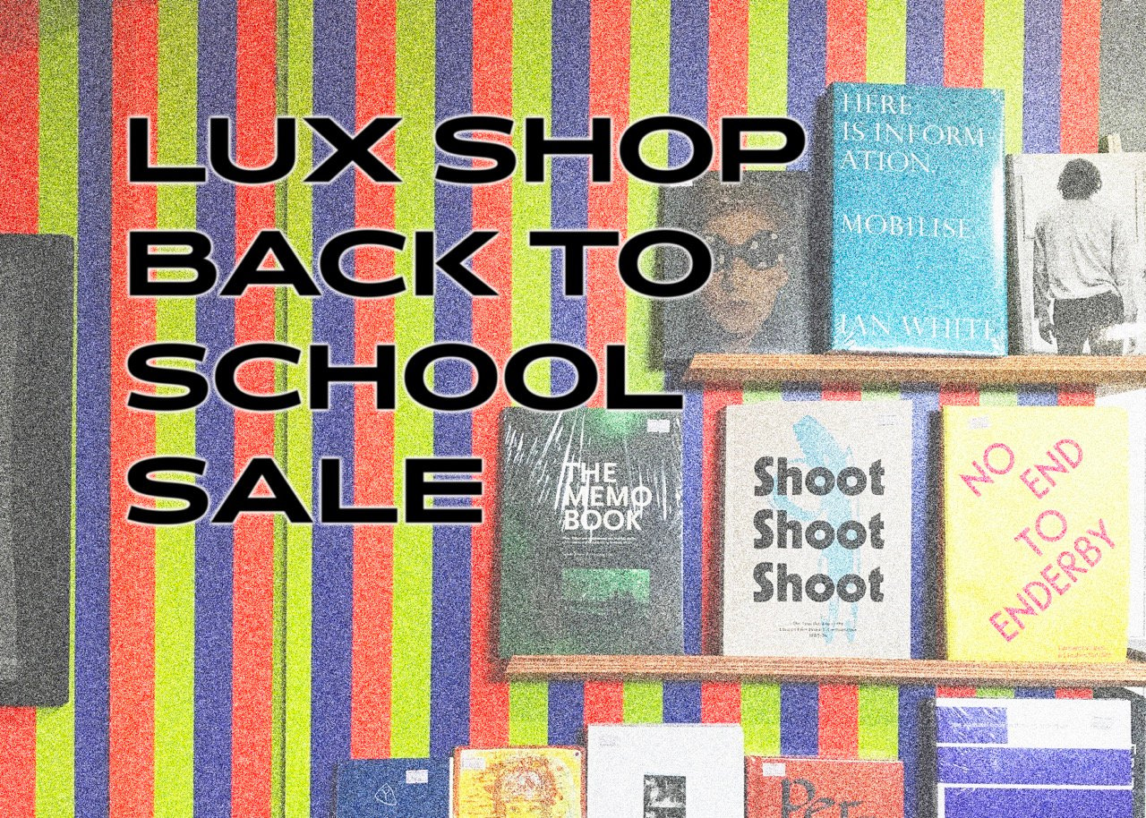 A black caption with white outlines that reads 'LUX Shop Back to School Sale' against a faded, grainy image featuring colorful stripes and three tiers of book displays