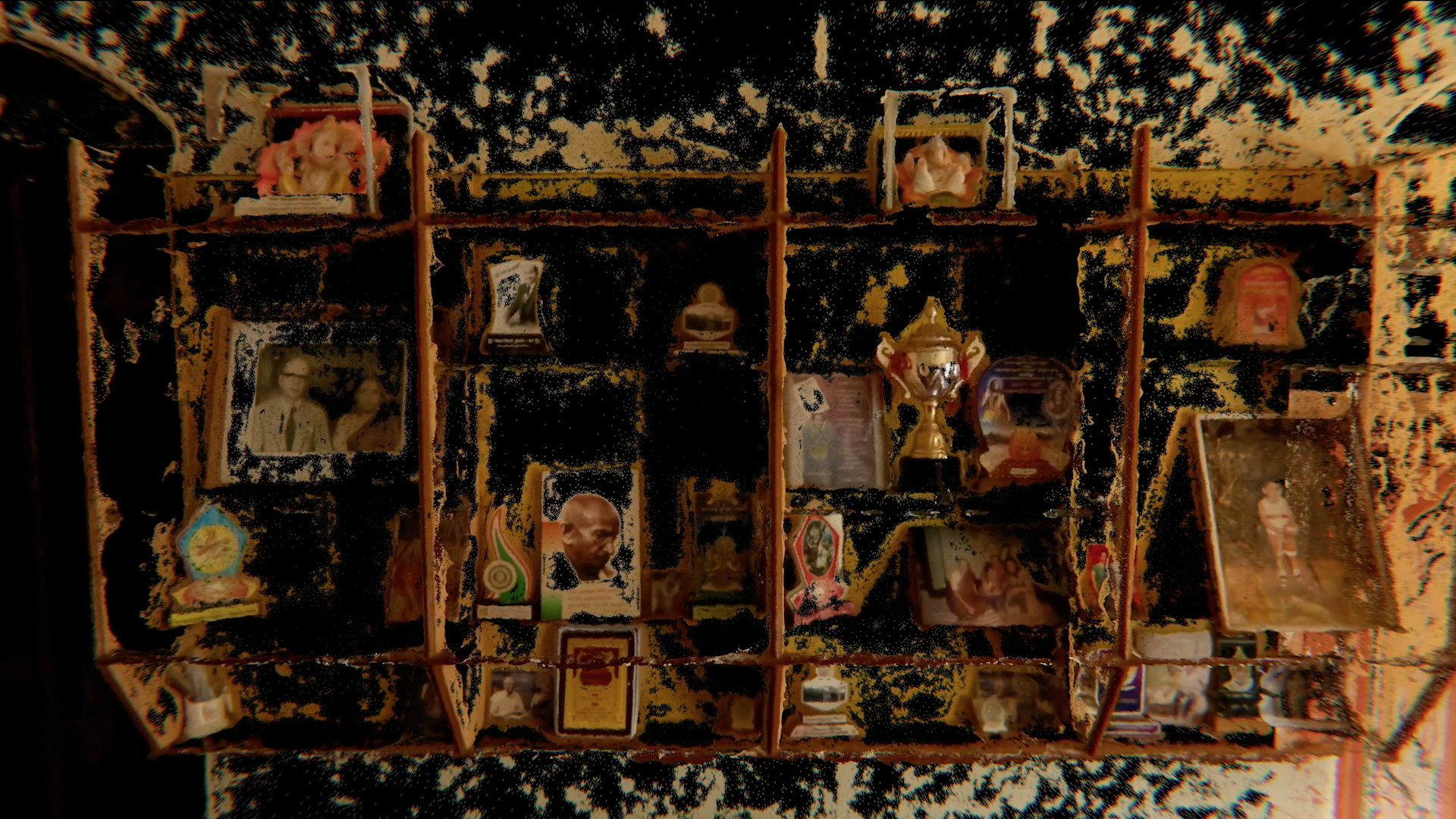 On a wooden shelving unit, a diverse collection of items is showcased, comprising family photographs, postcards, and various objects such as a small gold trophy. The image undergoes digital manipulation, where sections have been selectively blacked out with a painterly effect.