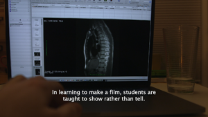 The inside of a body, including a spine and other organs, appears on a laptop screen. A white person's hand reaches toward the laptop's keyboard. On top of the hand, a caption reads: “In learning to make a film, students are taught to show rather than tell.”