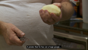 The torso of a white man holding a potato in one hand and a knife in the other. A caption at the bottom of the image reads: "A potato that he has cut a huge gouge..."
