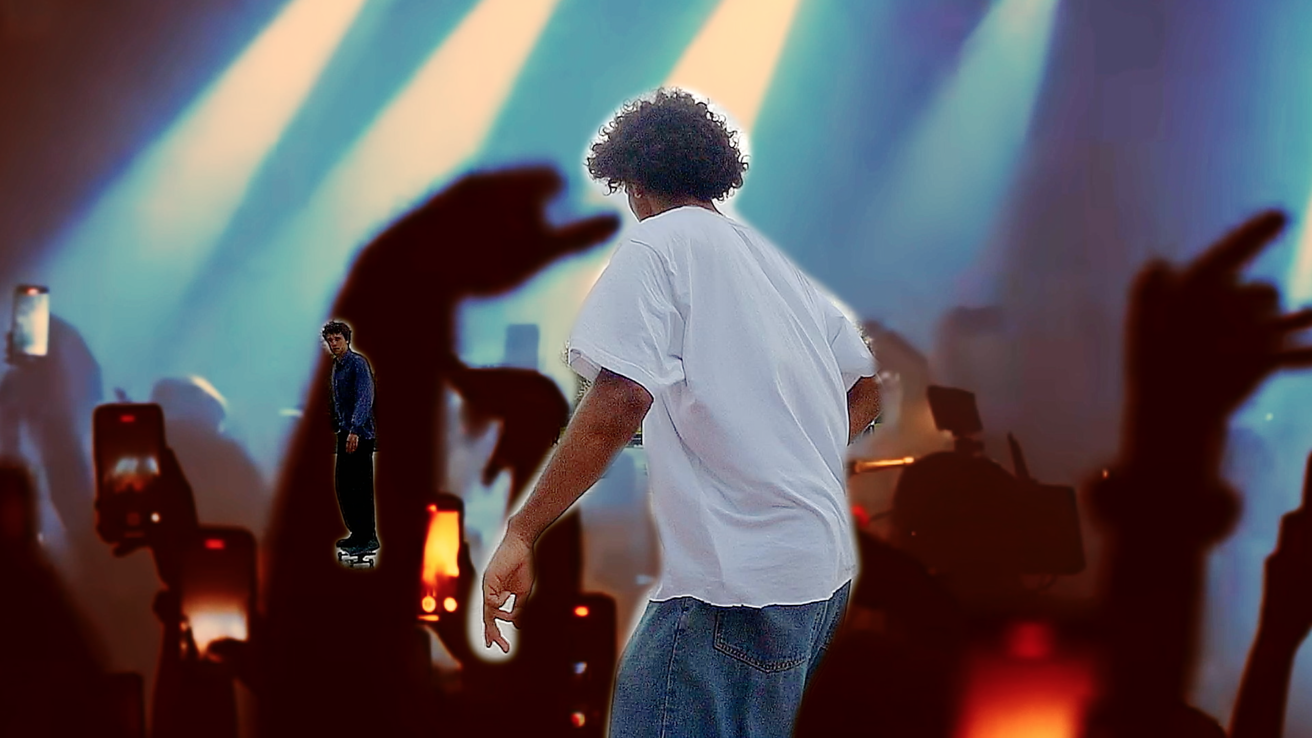 image of the back of a person in a white t-shirt and another person in the distance facing the viewer and they are on a skateboard. the background is a concert view of the performance and people holding up phones to record.