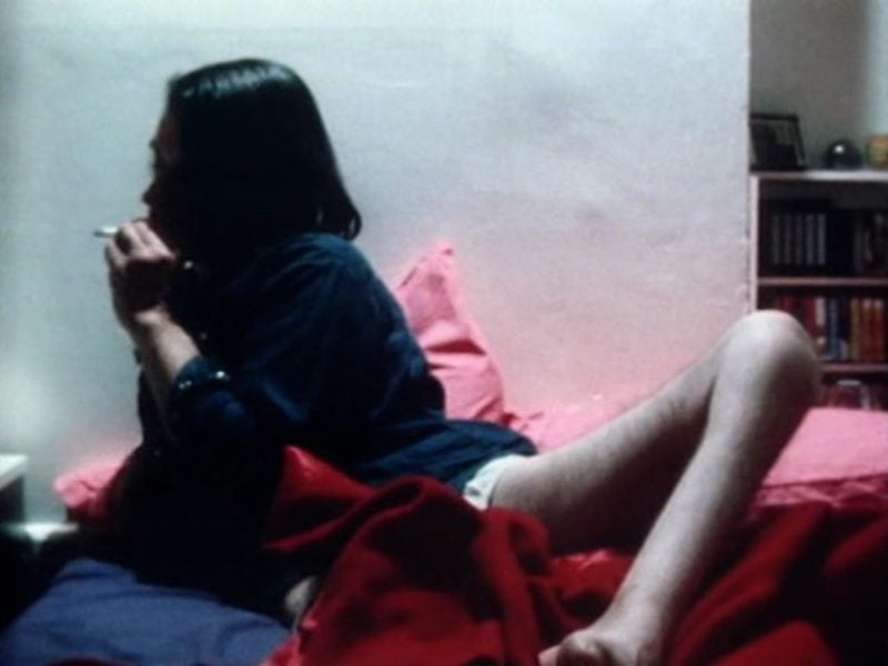A man is in a bed smoking and his one leg is exposed and visible over a blanket