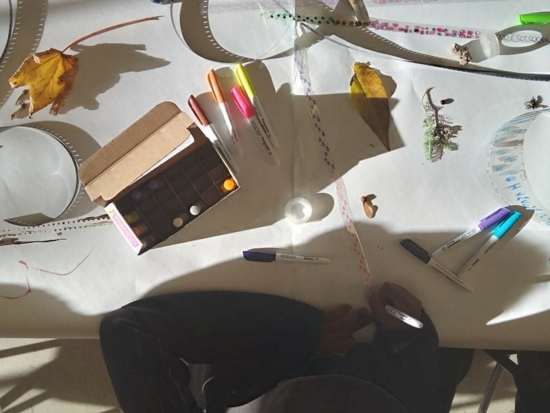 overhead view of two people drawing on film scripts on a table full of sharpies, film strips, leaves