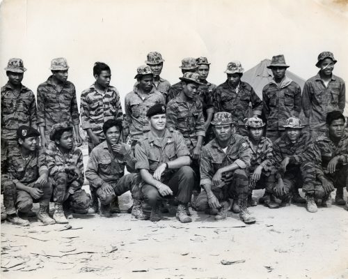 a still from the film Erase and Forget. A black and white image of soldiers posing for the camera in the centre is a white man, Bo Gritz the subject of the film, he is surrounded by black soldiers.