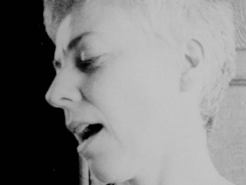A profile of a white woman's head fills the frame as a grainy B&W image. The woman looks down and opens her mouth slightly.
