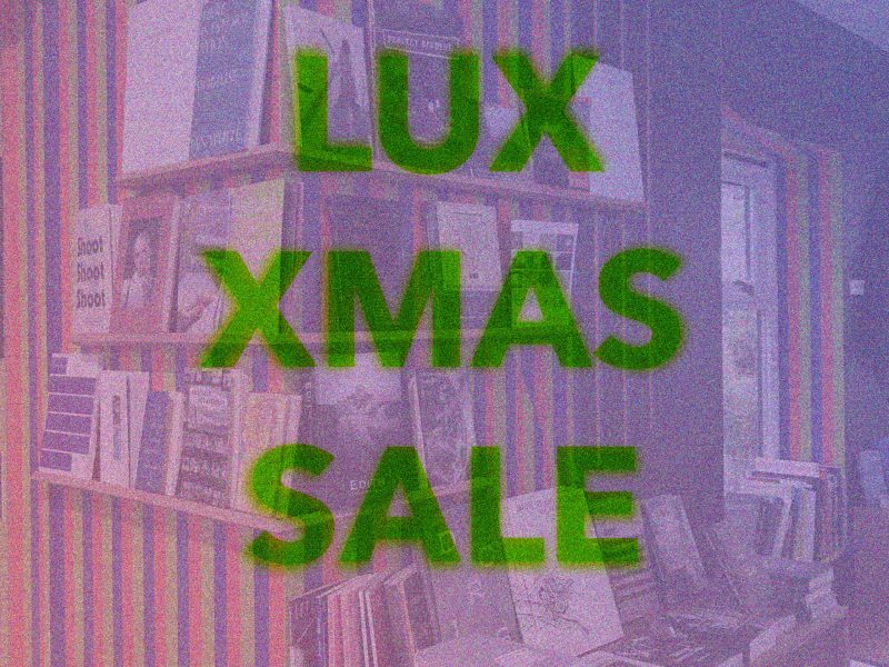 green transluscent text LUX XMAS SALE overlays a pink filtered image of a bookshop whose walls are painted in strips and decorated with book displays.