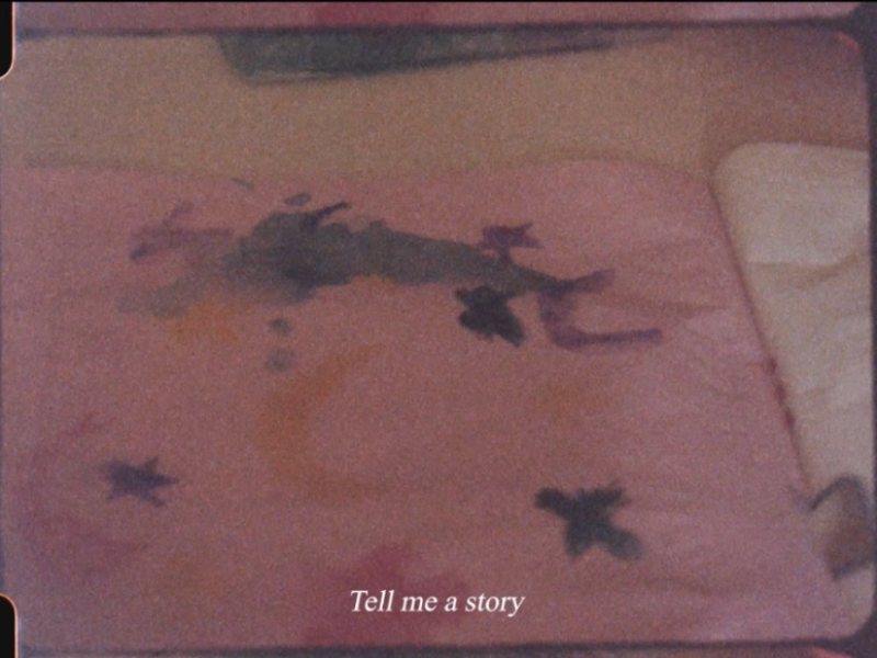 Grainy 16mm film still of a watercolour drawing of birds and moons on pinkish paper. Caption at the bottom reads: Tell me a story