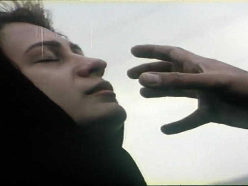 A woman in a hijab with her head slightly tilted back, eyes closed, and a serene expression. A hand stretches into the frame, as if reaching towards the woman's face