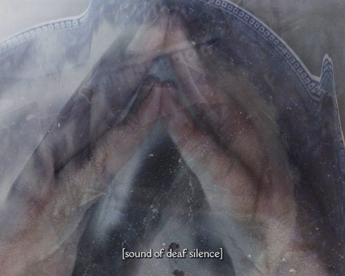 Two hands pressed together, with fingers interlocked. They are enveloped by a blue and white ceramic plate, with a distorted effect. The image of the plate is duplicated in another transparent layer. Caption says “Sound of Deaf Silence”