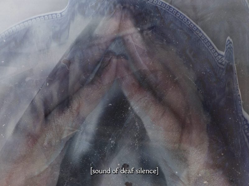 Two hands pressed together, with fingers interlocked. They are enveloped by a blue and white ceramic plate, with a distorted effect. The image of the plate is duplicated in another transparent layer. Caption says “Sound of Deaf Silence”