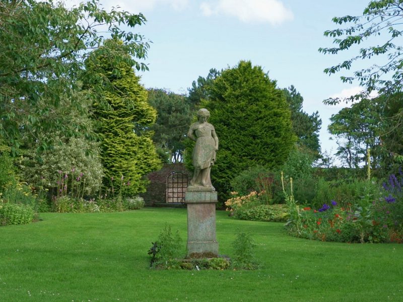 A beautifully cultivated garden. At the centre is a statue of a woman on a podium.
