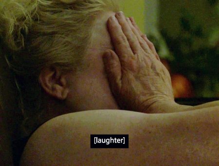 In a dimly lit room, a white woman with blonde hair covers her face with her hands. Her eyes appear to be closed tightly; it's unclear if she's laughing or crying. A caption at the bottom of the image reads: “laughter.”