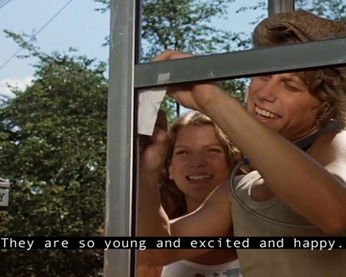 Liza Sylvestre, Captioned-Channel Surfing  (still), 2016. Courtesy: the artist
[Image description: Movie still, close-up of a white man and woman wearing summer clothes in a rural setting looking excited in a phone booth. A caption reads “They are so young and excited and happy.”]