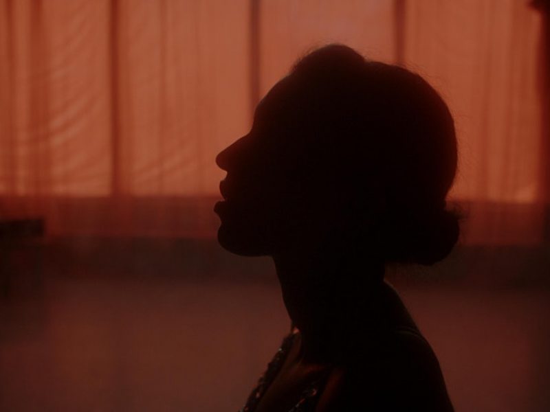 A silhouette of a person stands in front of warm atmospheric lighting coming through the translucent window curtain.