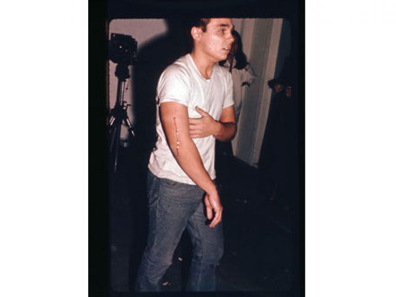'At 7:45 p.m. I was shot in the left arm by a friend. The bullet was a copper jacket .22 long rifle. My friend was standing about fifteen feet from me'. November 19, 1971, Chris Burden, 1971, performance at F Space, Santa Ana, CA. Photo courtesy of University of California, Berkeley Art Museum