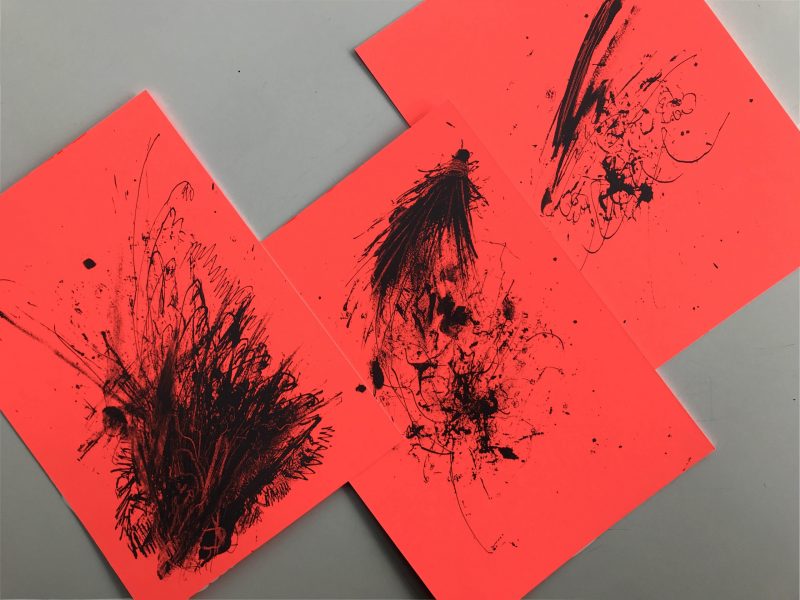 Flatlay of scratchy drawings in black ink printed on red fluorescent papers. Drawings resemble spilled and smudged black ink.