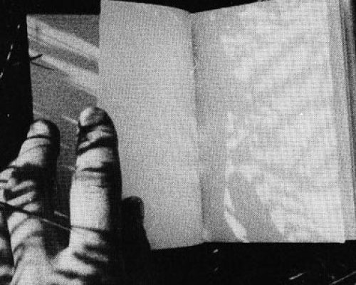 a black and white image of a book being held open by a hand, shadows fall across the page