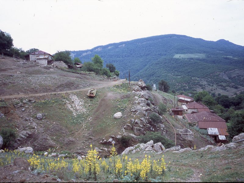 image from the film Black Bach Artsakh (2021), a tank is parked in the middle distance on the side of a hill, it is incongruous in a peaceful rural setting